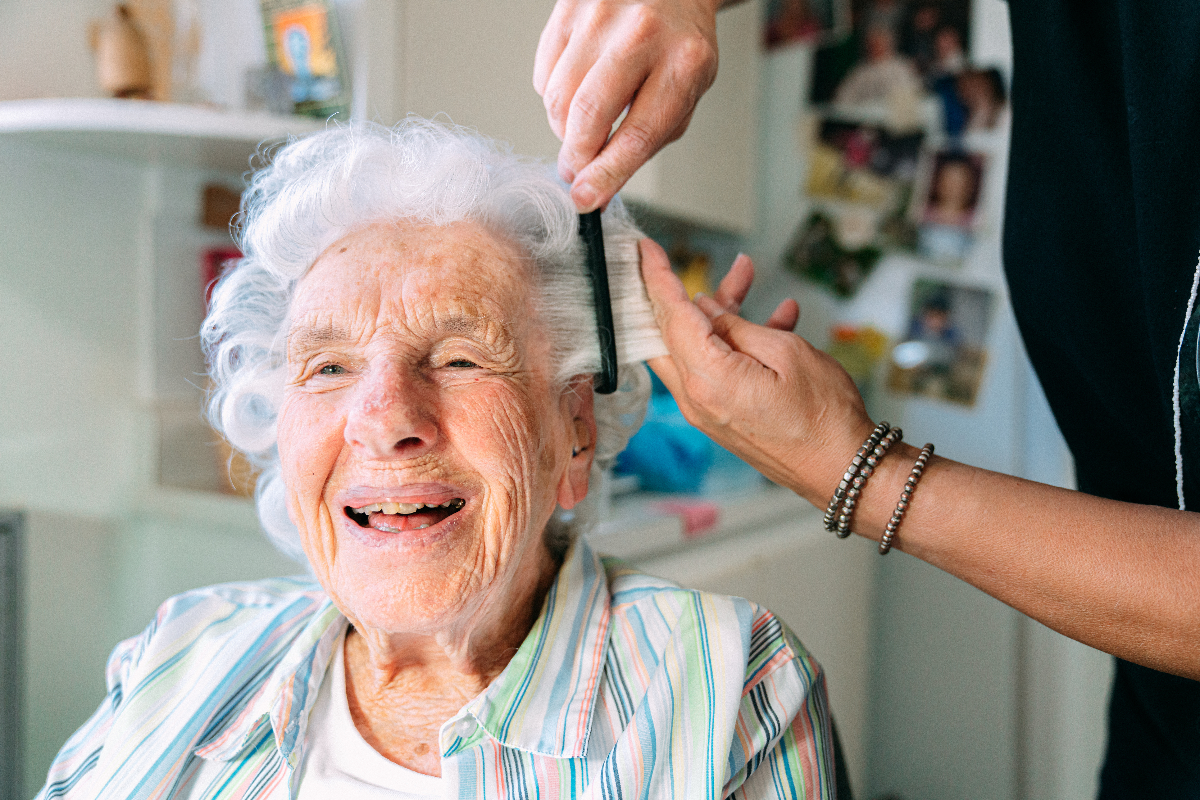 A laughing resident has her hair cut and styled by a hairdresser.